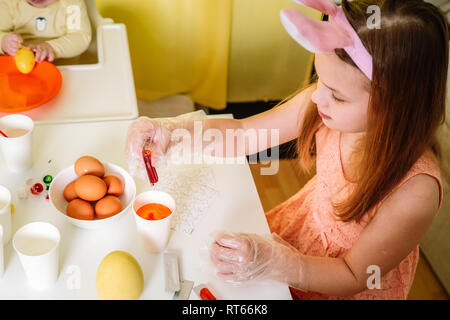 Carino bambina indossa orecchie di coniglietto e vernici di uova di Pasqua in ambienti interni Foto Stock