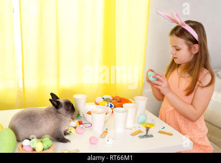 Carino bambina indossa orecchie di coniglietto e vernici di uova di Pasqua in ambienti interni Foto Stock