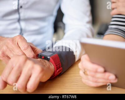 Close-up di imprenditore e imprenditrice con smartwatch e tablet in ufficio Foto Stock