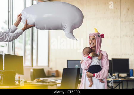 Giovane madre in unicorn onesie, tenendo il suo figlio nelle sue braccia con il discorso di bolla sopra la sua testa Foto Stock