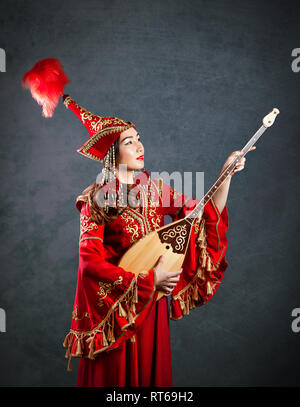 Il kazako donna in costume rosso giocando dombra kazako strumento musicale a sfondo grigio Foto Stock