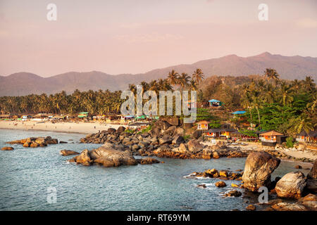 Bellissima vista del tramonto tropicale spiaggia con bungalow e palme di cocco a Palolem in Goa, India Foto Stock