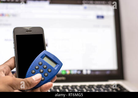 Mano che tiene il telefono e internet security key e carta bancomat con monitor mostra transazione internet come sfondo Foto Stock
