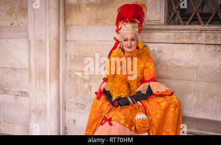 Donna mascherata con un bel colore arancione costume durante il carnevale di Venezia Foto Stock