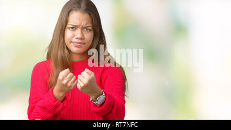 Giovane bella bruna donna che indossa inverno rosso maglione su sfondo isolato pronti a lottare con pugno gesto di difesa, arrabbiato e sconvolto il viso, AFR Foto Stock