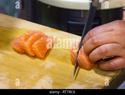 Le mani di taglio di pesce Salmone su tavola di legno, tagliata a fette di salmone per il nigiri sushi Foto Stock