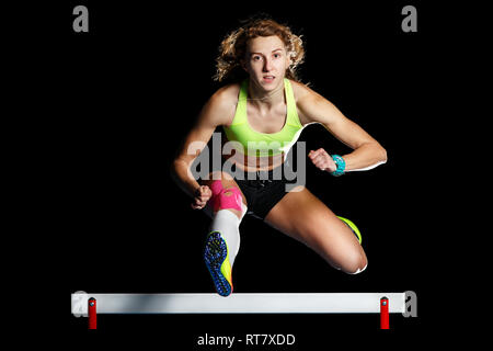 Giovane atleta femminile saltando ostacoli a sprint. Sprinter saltando ostacolo isolato su sfondo nero Foto Stock