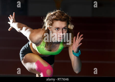 Atleta femminile a partire da gara sprint in esecuzione da blocchi su sfondo nero Foto Stock