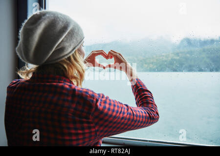 Il Cile, Hornopiren, donna sagomatura di un cuore con le mani in corrispondenza della finestra di un traghetto Foto Stock