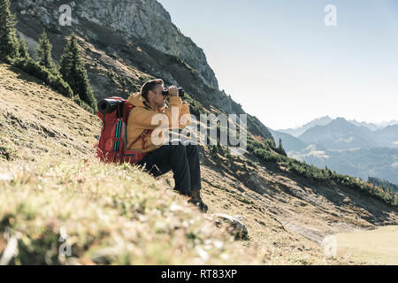 Austria, Tirolo, uomo avente una pausa durante un escursione in montagna cercando attraverso il binocolo Foto Stock