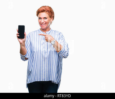 Accattivante senior redhead caucasica donna che mostra lo schermo dello smartphone su sfondo isolato molto felice puntando con mani e dita Foto Stock