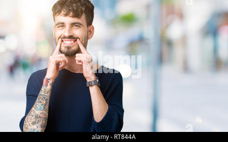 Giovane uomo bello su sfondo isolato sorridente con la bocca aperta, le punte delle dita rivolte e costringendo il sorriso allegro Foto Stock