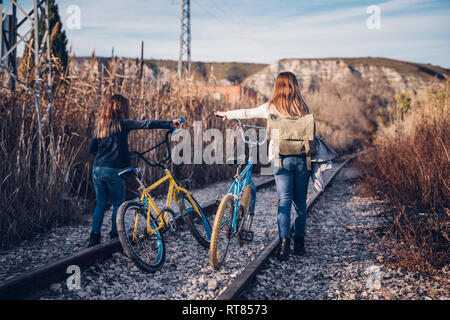 Due ragazze di camminare sulla via treno con le biciclette Foto Stock