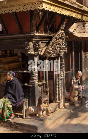 Il Nepal, Valle di Kathmandu, Bhaktapur, Bangsagopal Nasamana, vecchio uomo e donna seduta nella luce del sole al di fuori, riccamente intagliato di legno vecchio tempio Foto Stock