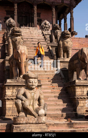 Il Nepal, Valle di Kathmandu, Bhaktapur, Taumadhi Tole, Tempio Nyatapola, il turista in posa sui passi accanto a statue Foto Stock