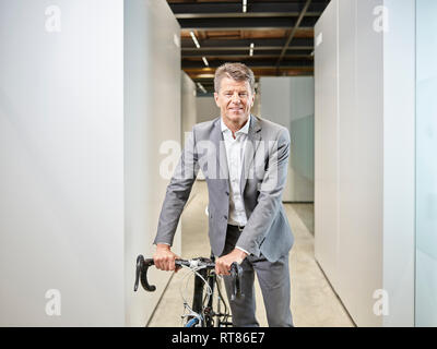 Ritratto di imprenditore sorridente con la bicicletta sul pavimento per ufficio Foto Stock