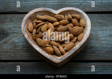 Le mandorle in un cuore di legno piatto sagomato Foto Stock