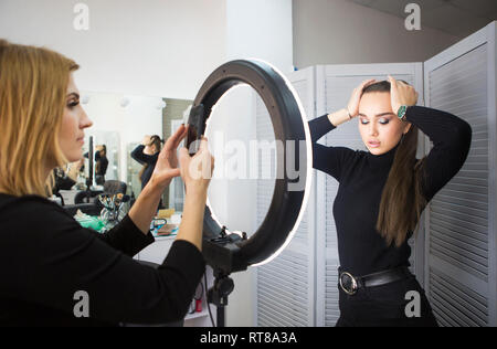 Make up Artist tenendo mobile photo per il modello con il trucco Foto Stock