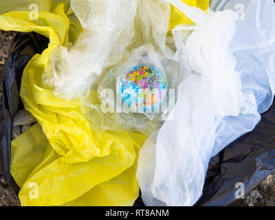 Un globo terrestre o pianeta terra tra la spazzatura e sacchetti di plastica. Concetto di ecologia Foto Stock