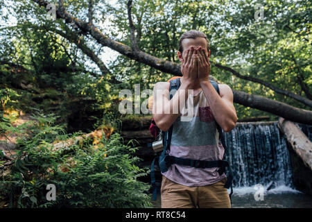 Giovane uomo con zaino rinfrescante in acqua in una foresta Foto Stock
