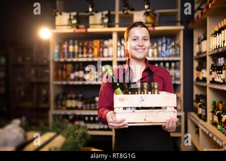 Foto di felice brunette venditore con scatola di legno con il vino in negozio Foto Stock