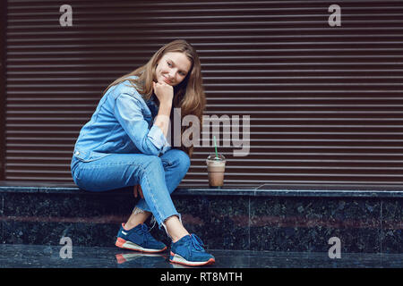 Ragazza bionda sorridente seduto con cocktail in una tazza di plastica Foto Stock