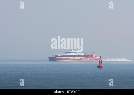 Imbuto Rosso gruppo, un catamarano ad alta velocità (SeaCat), Rosso Jet 7, lascia un banco di nebbia di mare come essa si accosta al Porto di Southampton, Hampshire, Regno Unito. Foto Stock