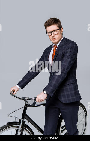 Imprenditore elegante posa con bicicletta isolato su grigio Foto Stock