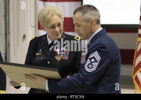 Master Chief Sgt. Winfield Hinkley, senior arruolato leader dell'Alaska National Guard, presenta il Mag. Gen. Laurie Hummel, ex aiutante generale dell'Alaska Guardia Nazionale e Commissario del Dipartimento Militare e Veterans Affairs, con una replica dell'assetto organizzativo dei colori durante la sua cerimonia di pensionamento presso il National Guard armory su base comune Elmendorf-Richardson, Alaska, Gennaio 26, 2019. Hummel è servita come aiutante generale dal febbraio 5, 2015 attraverso dic. 28, 2018. Foto Stock