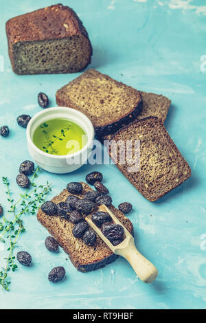 Greco tradizionale antipasto italiano olive nere essiccate con pane e olio di oliva servita su un calcestruzzo blu tabella sullo sfondo di superficie Foto Stock