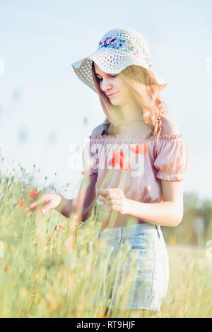 Beautieful giovane ragazza nel campo dei fiori selvatici. Ragazza adolescente picking i fiori di primavera nel prato che indossa un cappello e abiti estivi. La spesa tim Foto Stock