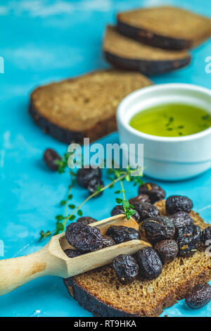 Greco tradizionale antipasto italiano olive nere essiccate con pane e olio di oliva servita su un calcestruzzo blu tabella sullo sfondo di superficie Foto Stock