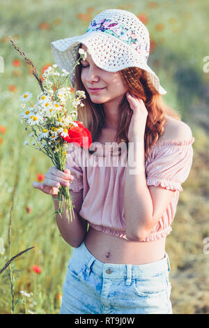 Beautieful giovane ragazza nel campo dei fiori selvatici. Ragazza adolescente picking i fiori di primavera nel prato, tenendo bouquet di fiori. Lei indossa hat Foto Stock