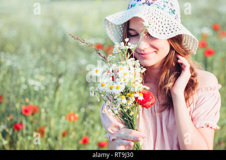 Beautieful giovane ragazza nel campo dei fiori selvatici. Ragazza adolescente picking i fiori di primavera nel prato, tenendo bouquet di fiori. Lei indossa hat Foto Stock