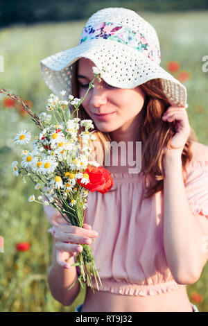 Beautieful giovane ragazza nel campo dei fiori selvatici. Ragazza adolescente picking i fiori di primavera nel prato, tenendo bouquet di fiori. Lei indossa hat Foto Stock