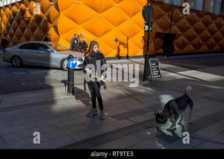 Una donna si ferma per consentire il suo cane ad annusare il terreno di fronte alla temporanea accaparramento di rinnovamento del marchio di lusso di Louis Vuitton a New Bond Street, il 25 febbraio 2019, a Londra, in Inghilterra. Foto Stock