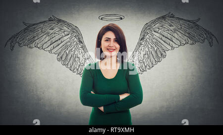 Positivo donna fiducioso con le braccia incrociate sorridente largamente immaginare se stessa un angelo con soffici ali dietro la schiena e un alogeno sopra la testa. Super power Foto Stock