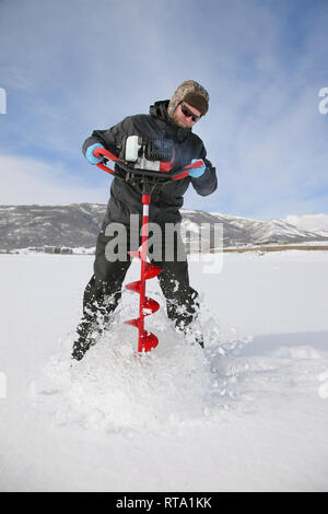 Adulto pescatore di ghiaccio di praticare un foro nel ghiaccio con un lago con una coclea di alimentazione Foto Stock