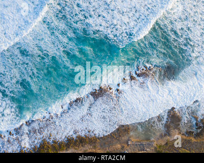 Antenna fuco shot che mostra l'oceano onda e si rompe sulla costa rocciosa dall'alto. Foto Stock