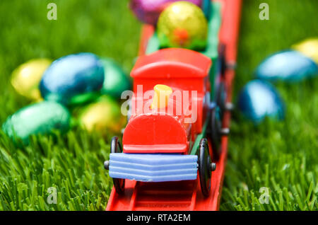 Primo piano della luminosa giocattolo di plastica treno sulle vie di trasporto uova di Pasqua. Divertimento gioioso della Pasqua tema del viaggio, infanzia, uova di pasqua e giocare. Foto Stock