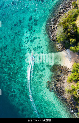 Vista da sopra, vista aerea di una tradizionale barca long-tail vela vicino a una splendida barriera corallina con una piccola e bella spiaggia. Foto Stock