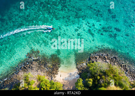 Vista da sopra, vista aerea di una tradizionale barca long-tail vela vicino a una splendida barriera corallina con una piccola e bella spiaggia. Foto Stock