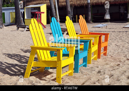 Quattro luminose colorate sedie Adirondack nella sabbia Foto Stock