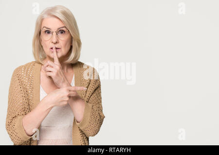 Vecchia donna tenendo premuto il dito su i labbri rivolti a copyspace isolato Foto Stock