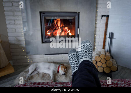 La masterizzazione di camino e un uomo in piedi in calze di lana sul primo piano. Concetto di Hygge Foto Stock