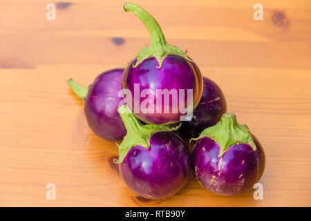 Grande angolo di inquadratura ravvicinata di un mazzetto di rotondo piccolo viola melanzane tailandesi (Solanum melongena), impilate una sull'altra su di un tavolo di legno. Foto Stock