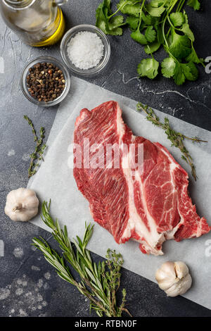 Primo fresco bistecca su bianco carta craft con rosmarino, cardamomo, aglio, olio d'oliva, sale e pepe su sfondo nero. Concetto di fresco e salutare Foto Stock