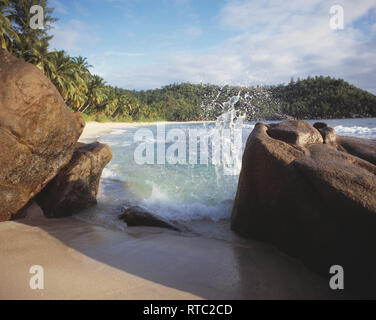 Le Seychelles. Mahé. Takamaka. Spiaggia scena con spruzzi d'onda sui massi. Foto Stock