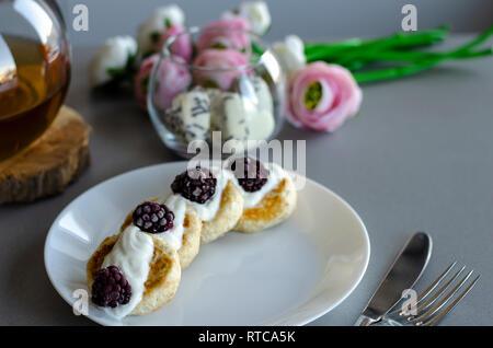 In casa di ricotta frittelle con panna acida e more per la prima colazione. La dieta alimentare e mangiare sano concetto. Foto Stock