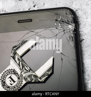 Il vetro rotto sullo schermo del telefono e un dollaro a forma di chiave, come un concetto di costo di riparazione di un dispositivo mobile, vista dall'alto Foto Stock